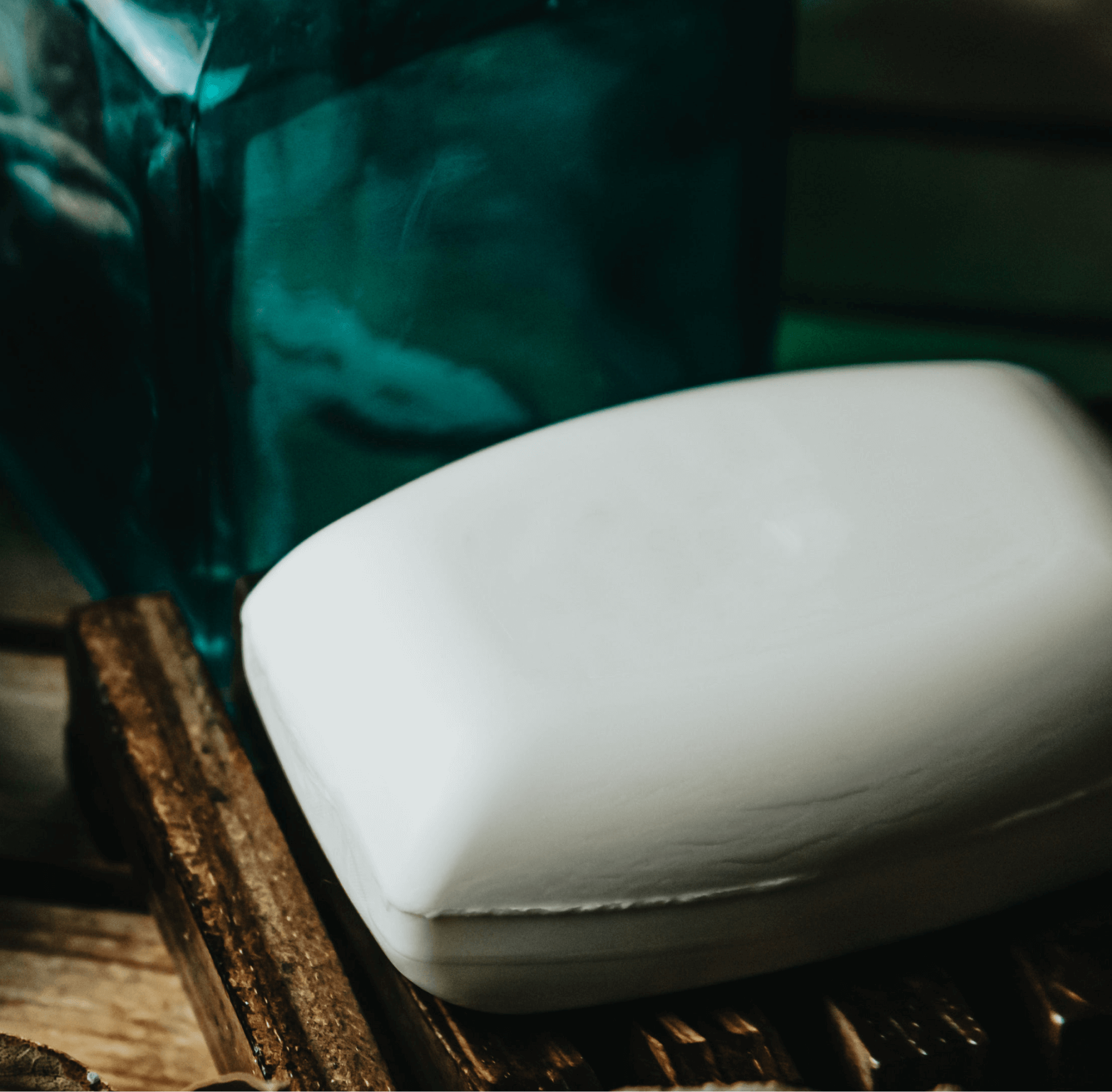 White bar of soap on a wooden surface with a green cloth in the background